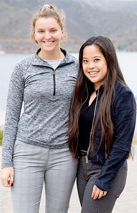 Nancy Bush and Caitlin Dinh stand on a paved drive with a Catalina Island harbor in the background.