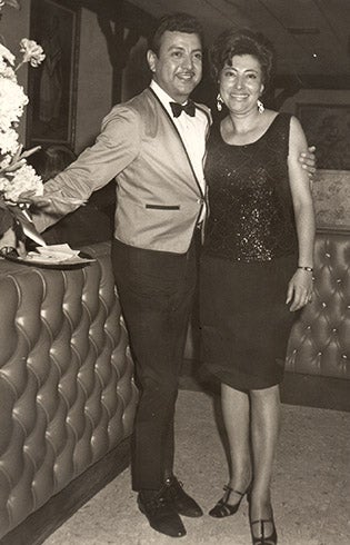 Black and white photo of a waiter standing with his arm around a well-dressed woman.