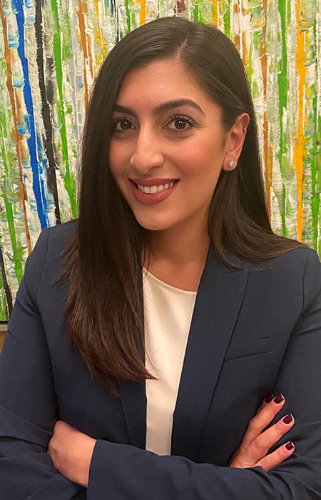 Portrait of Yasmin Fardghassemi standing arms crossed in front of a multi-colored background.