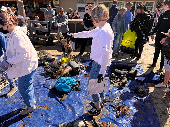 Volunteers stand around and among debris and dirt on a blue tarp.