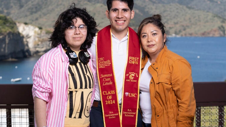 student wearing a graduation sash and their guests with Wrigley Marine Science Center's waterfront as the background