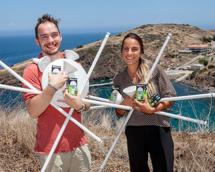 two students, standing on a hill overlooking the WMSC campus, hold armfuls of the LED bulbs used to making campus light fixtures more energy-efficient