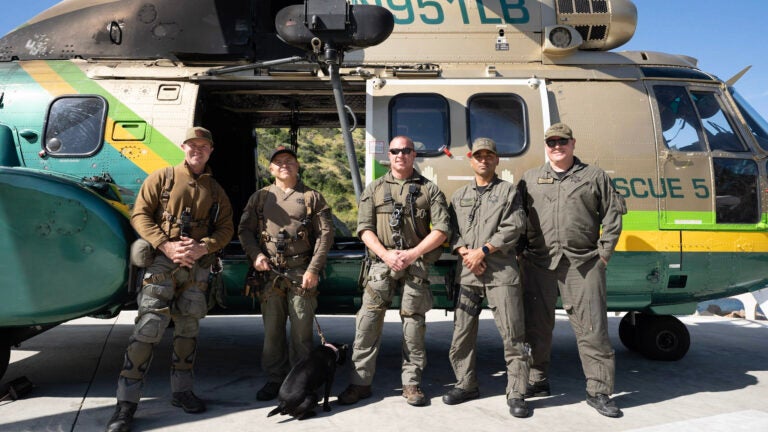 5 sheriffs and a black lab stand posed next to a rescue helicopter
