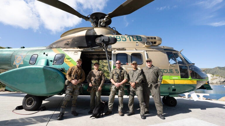 5 sheriffs and a black lab stand posed next to a rescue helicopter