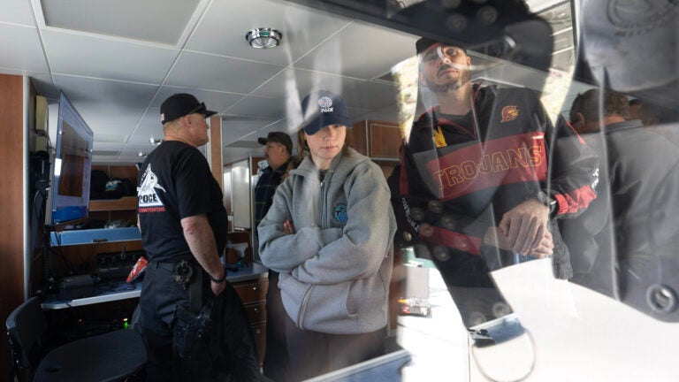 A group of people are looking into a glass box from which the camera shot is taken while examining equipment on the lower level of a ship