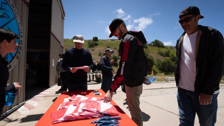 A group of people look at flags and pens displayed on a table outside the Catalina hyperbaric chamber