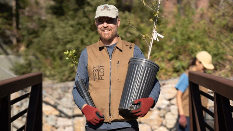 Alexander Robinson holds two potted plants while wearing a vest that reads 