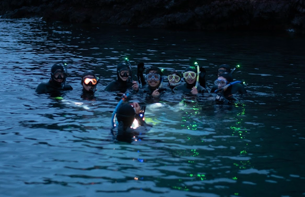 A group of students are snorkeling at night as different elements of their gear lights up