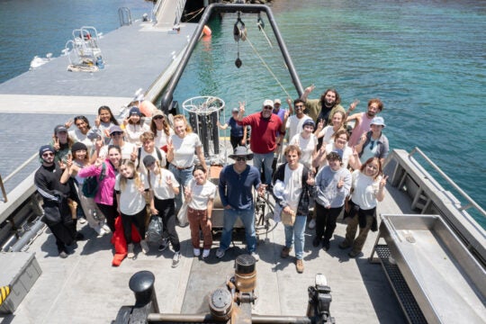 a group of students and their professor smile and hold up V-shaped 