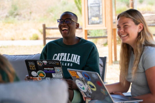 students holding laptops smile as they collaborate on a project