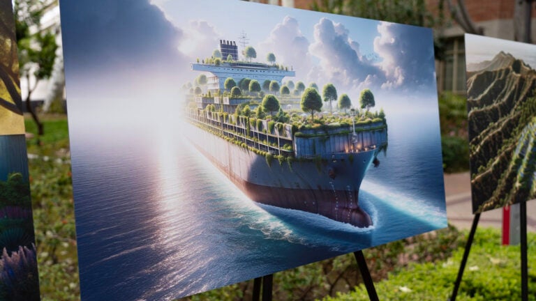 An AI-generated artwork sits on an easel in an outdoor courtyard. In the artwork, plants and trees cover the deck of a large cargo ship as it sails on the ocean.