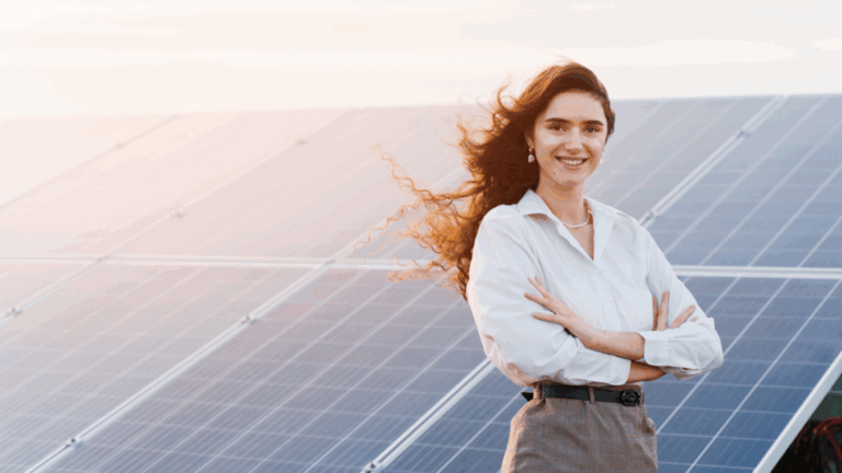 a smiling professional stands with crossed arms in front of a bank of solar panels