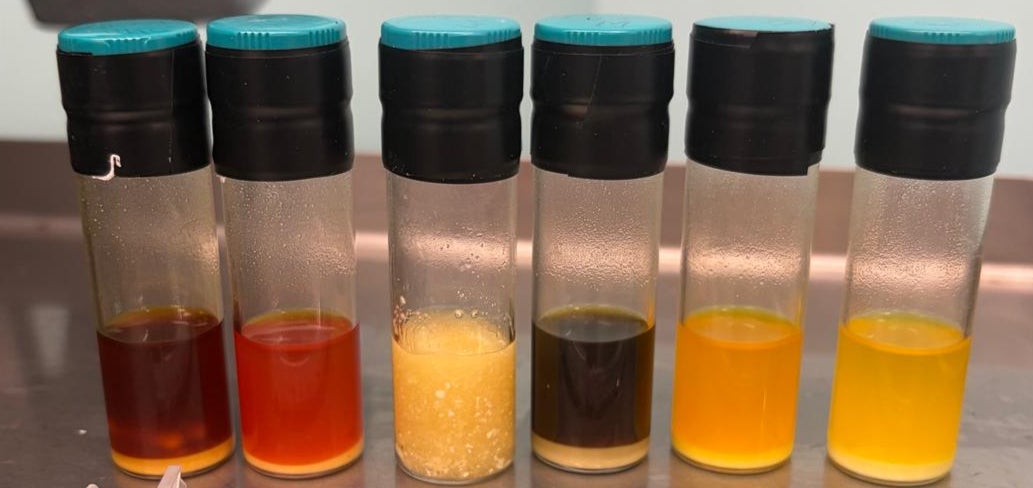6 clear cylinder containers containing various shades of red, yellow, and brown liquid