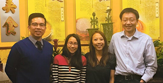 Chao Zhang posing with three students in a restaurant with Chinese characters
